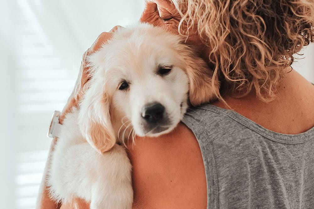 Woman holding a puppy on her shoulder, with the puppy looking sad, representing compassionate pet care.